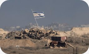 Área destruída com bandeira de Israel ao fundo