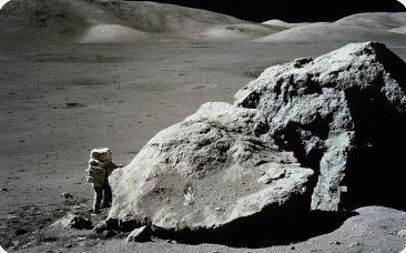 Astronauta junto a uma grande rocha na superfície lunar
