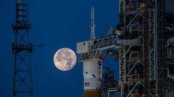 Foguete SLS na plataforma de lançamento com a Lua cheia ao fundo